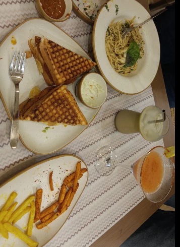 Genuine Kaaafi Korner table spread featuring grilled sandwiches, pasta, fries, and cold beverages